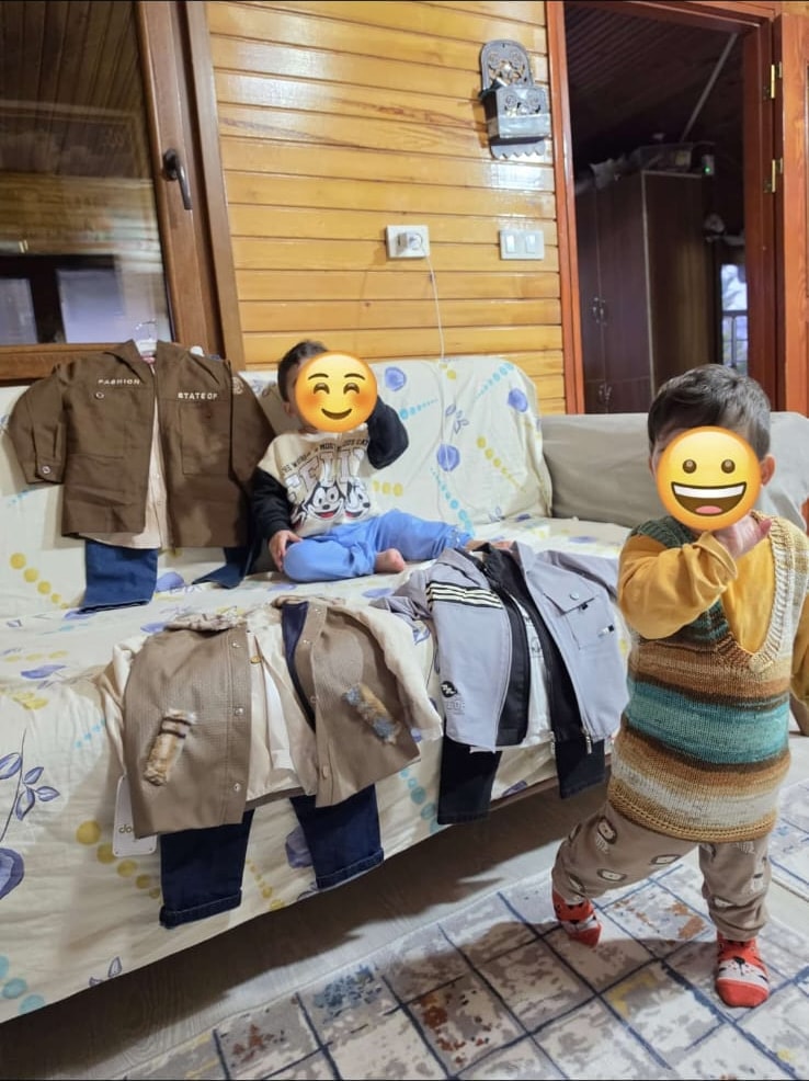 Evlerine ulaştırılan kışlık kıyafetlerin yanında duran iki çocuk
